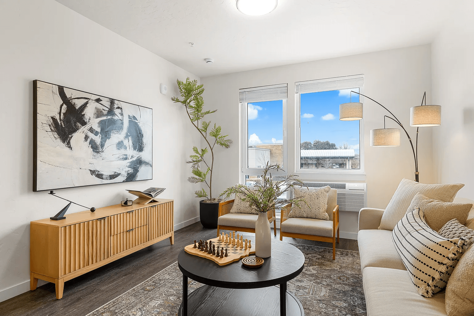 A living room with a large painting on the wall and a view of the outside through the window.